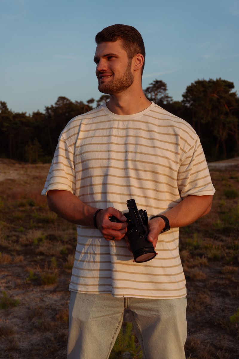 Persoon die met een videocamera in zijn handen staat kijken naar rechts, staand in een open veld.